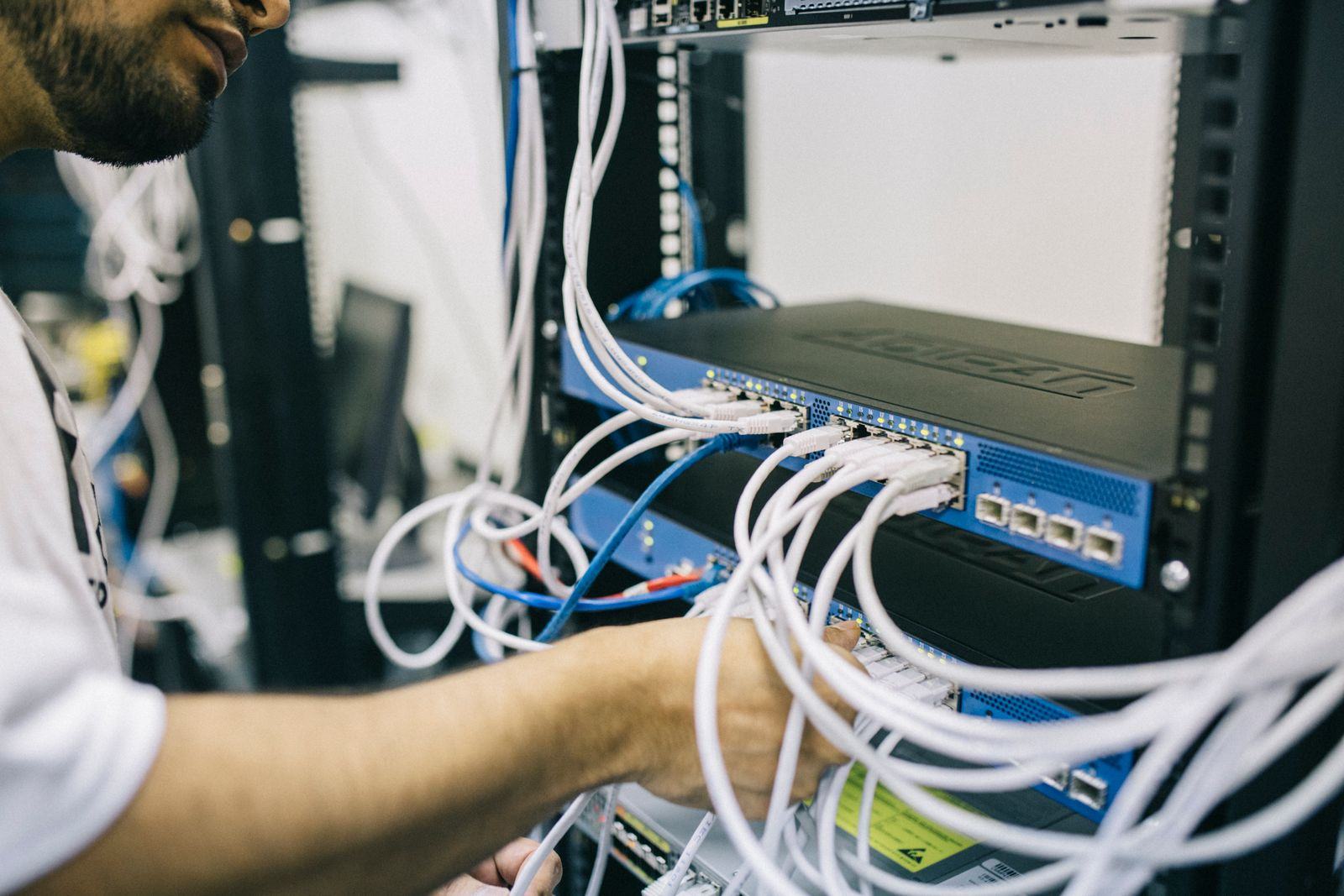 Engineer connecting network cables to a switch in a server rack